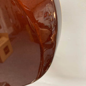 Close-up of a glossy brown curved surface—reminiscent of the 2009 Godin Summit CT w/Carved Flame Maple Cap electric guitar by Godin—with a visible scratch near the center, set against a plain white background.