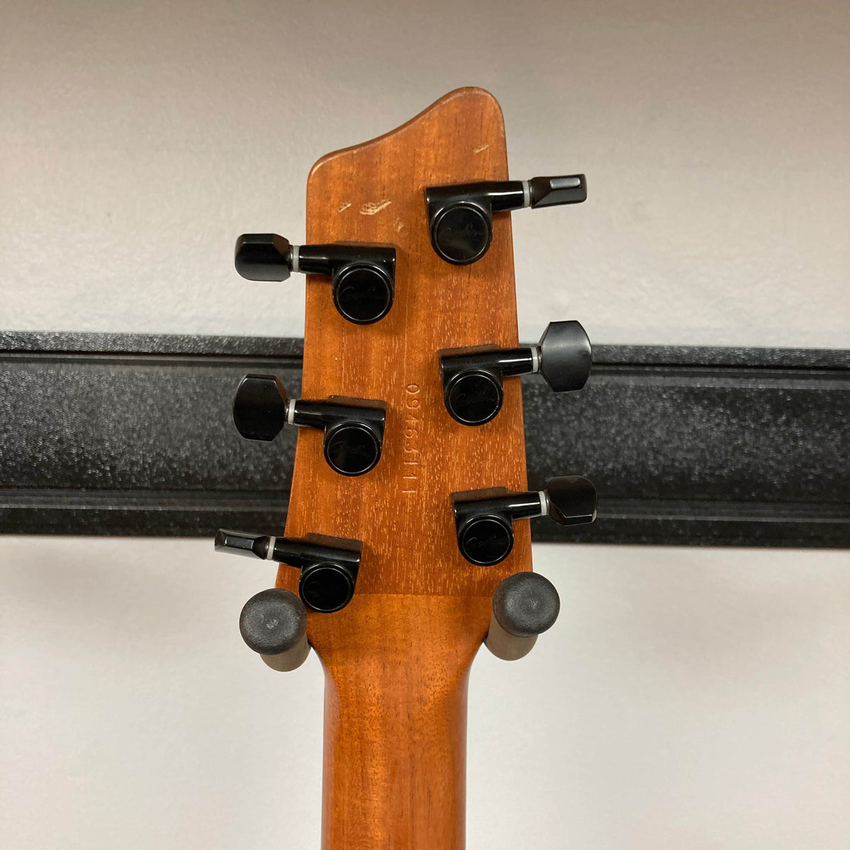 The back of a 2009 Godin Summit CT w/Carved Flame Maple Cap headstock features six black tuning pegs, highlighting the wooden neck of this electric guitar with a metal rail visible in the background.