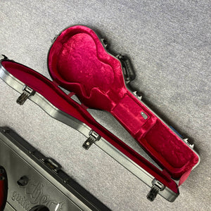 An open, empty Gator molded case with a red plush interior sits on a gray carpet, perfect for your 2025 Gibson Les Paul Studio Modern in Smokehouse Satin by Gibson. Another closed case rests nearby.