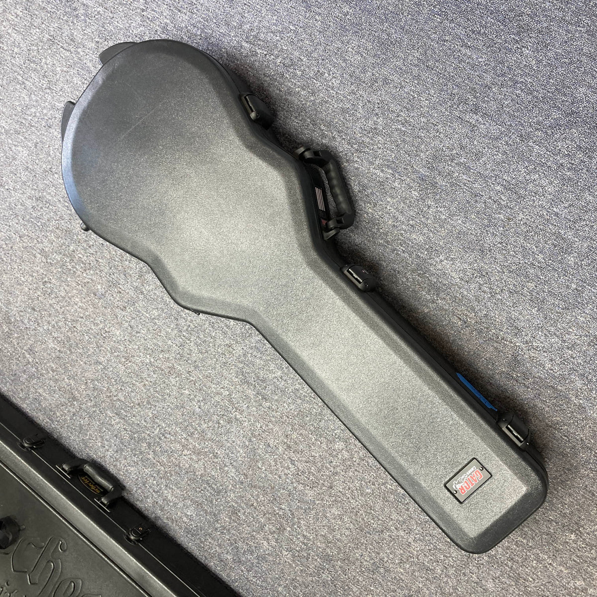 A Gator molded case for the 2025 Gibson Les Paul Studio Modern in Smokehouse Satin by Gibson lies closed on a gray carpeted floor.