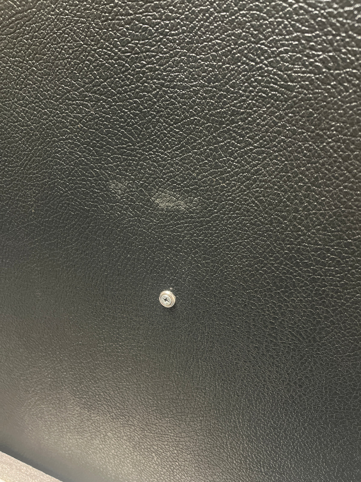 Close-up of a black textured surface—evocative of a vintage Marshall 1969 4x12 Cabinet with matching Celestion T1281 Greenbacks—featuring a small metal screw in the center and a faint smudge above it.