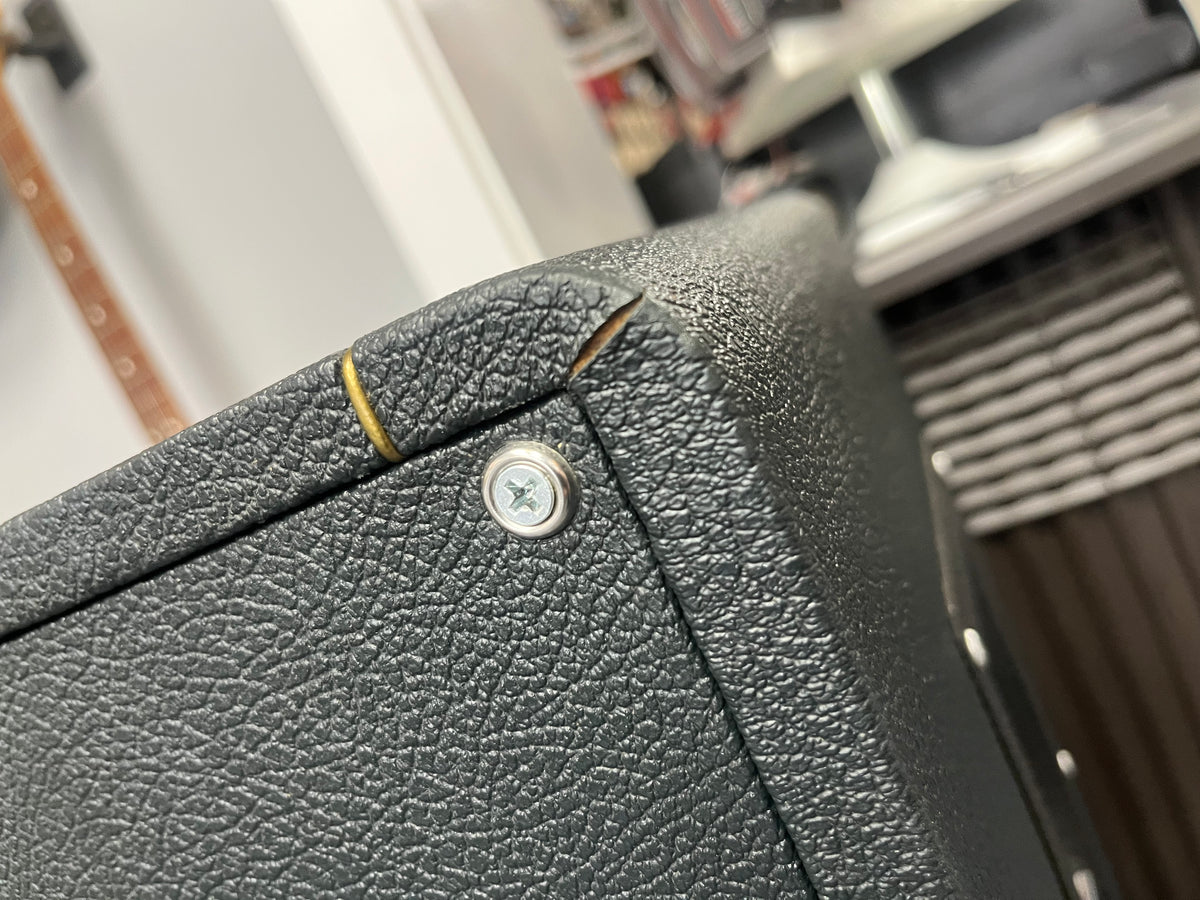 Close-up of a textured black 1969 Marshall 4x12 Cabinet with Matching Celestion T1281 Greenbacks, showing a visible crack near the corner and a metal screw. Shelves and objects are blurred in the background.