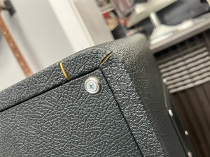 Close-up of a textured black 1969 Marshall 4x12 Cabinet with Matching Celestion T1281 Greenbacks, showing a visible crack near the corner and a metal screw. Shelves and objects are blurred in the background.