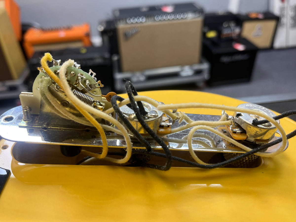 Close-up of wiring and components inside a Fender Custom Shop '51 Reissue Nocaster NOS 2006, with blurred guitar amps in the background—highlighting intricate details of this vintage-style Fender guitar.