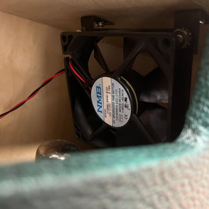 A close-up of a cooling fan with model info on the label, mounted inside a 2005 Divided by 13 RSA 31 Head with Matching 2x12 Cabinet and Flight Case by Divided by 13, with wires attached.