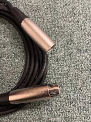 A coiled black American DJ MC-10 10ft XLR Microphone Cable with silver connectors rests on a textured light green surface—perfect for American DJ audio setups.