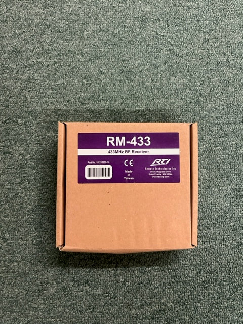 A brown cardboard box labeled "RTI RM-433 433MHz RF Receiver Module" by Remote Technologies Inc (RTI) sits on gray carpet. The label shows a barcode and "Made in Taiwan"—designed for easy integration with RTI control systems.