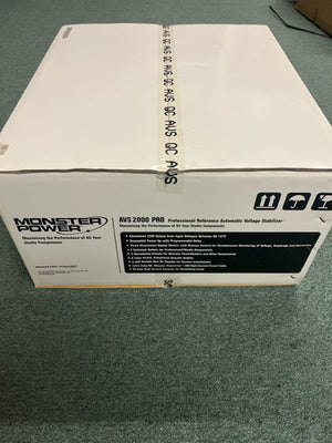 A white box labeled "Monster Power AVS 2000 PRO Professional Reference Automatic Voltage Stabilizer" by Monster Power sits on a green carpet, showing shipping symbols and product details on the side.