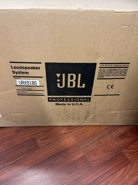 A cardboard box labeled "JBL Professional Loudspeaker System" sits on a wood floor, featuring the high-output VRX918S model for live sound reinforcement, with "Made in U.S.A." printed on the box.