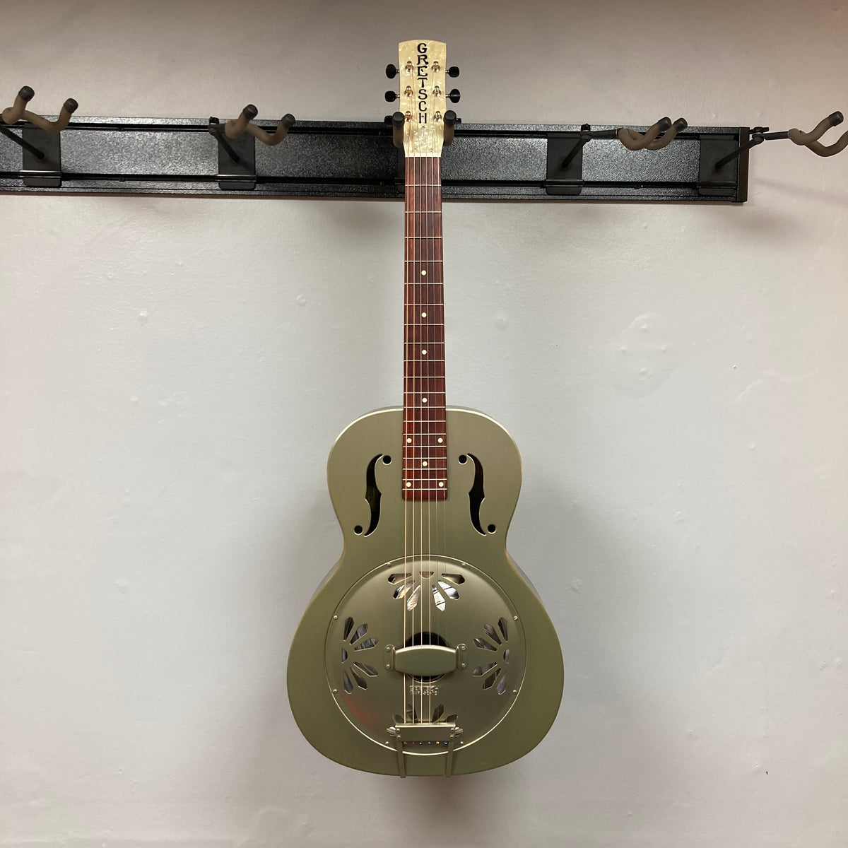 Gretsch G9201 Honey Dipper Round-Neck Resonator Guitar with brass body and distinctive resonator cone, displayed on a wall rack.
