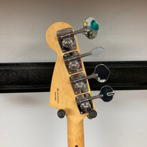 A Fender Mustang Player Bass PJ White Used with four metal tuning pegs on the headstock is displayed on a black wall hanger against a Polar White wall.