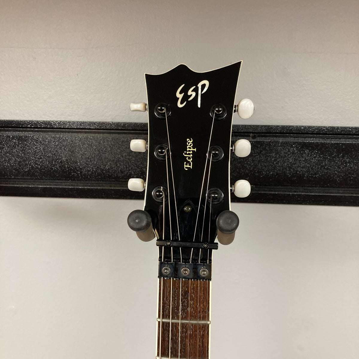 Headstock of an ESP Standard Eclipse Transparent Cherry Red guitar with tuning pegs and part of the fretboard visible, mounted on a wall hanger against a light background. Includes case. Brand: Esp.