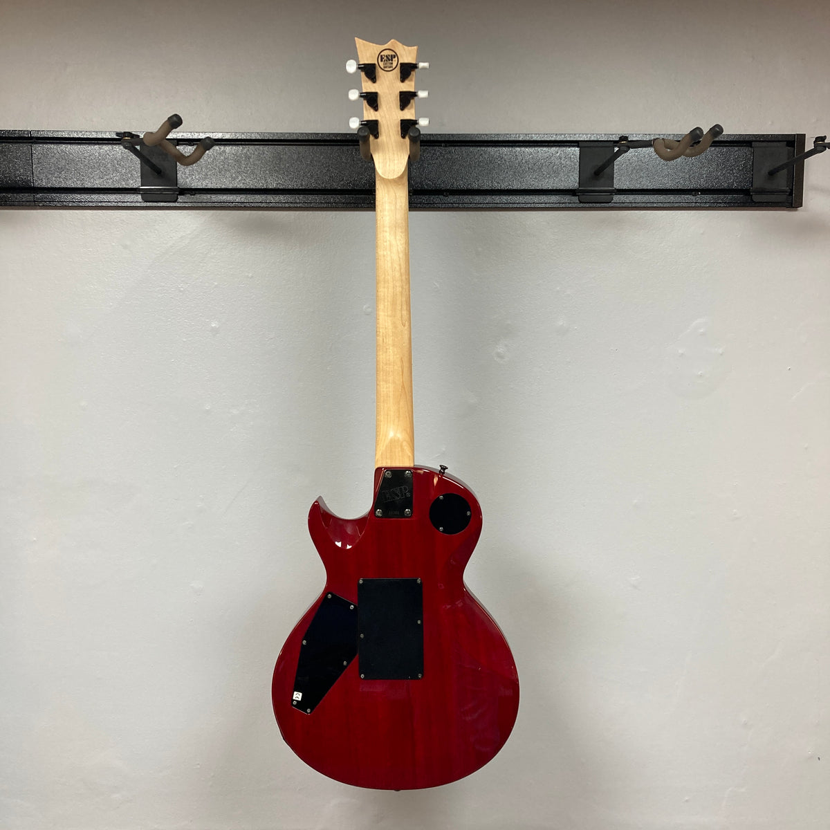 The ESP Standard Eclipse Transparent Cherry Red w/Case by Esp hangs on a wall-mounted rack, its back and neck displayed against a light-colored wall.