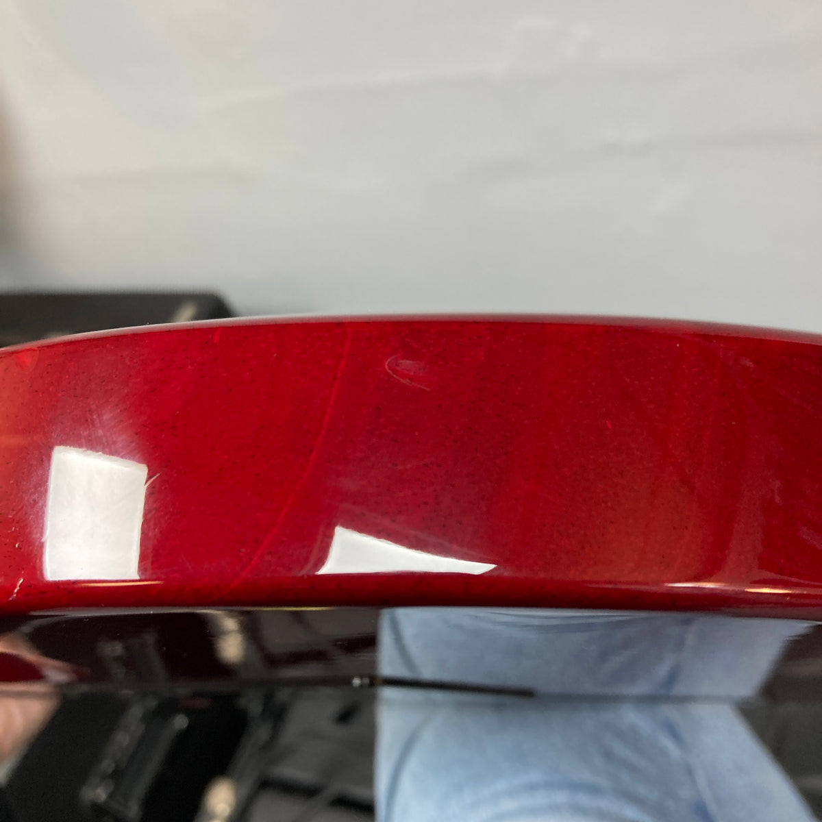 Close-up of the side edge of an ESP Standard Eclipse Transparent Cherry Red guitar body by Esp, showing minor surface scratches and reflections on its glossy finish; includes case.