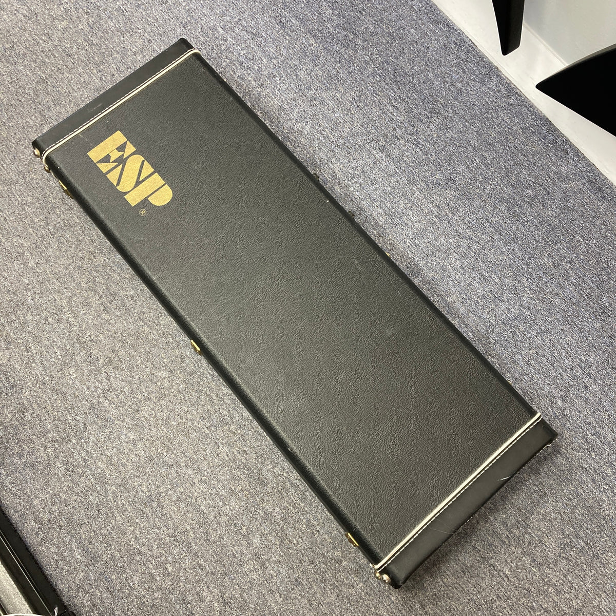 A black rectangular hard case with gold "ESP" lettering, designed for the ESP Standard Eclipse Transparent Cherry Red guitar by Esp, is shown resting on a gray carpeted floor.