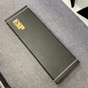 A black rectangular hard case with gold "ESP" lettering, designed for the ESP Standard Eclipse Transparent Cherry Red guitar by Esp, is shown resting on a gray carpeted floor.