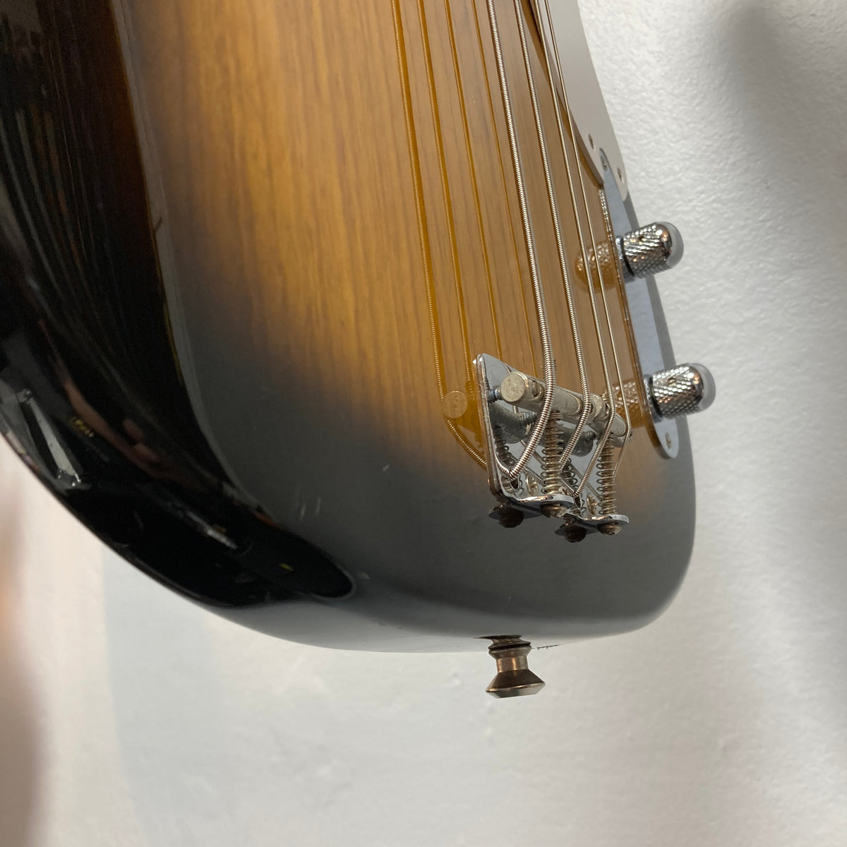 Close-up of the Fender Sting P Bass Sunburst bridge and strings, highlighting its chrome hardware against a white background—ideal for fans of vintage-style electric basses.