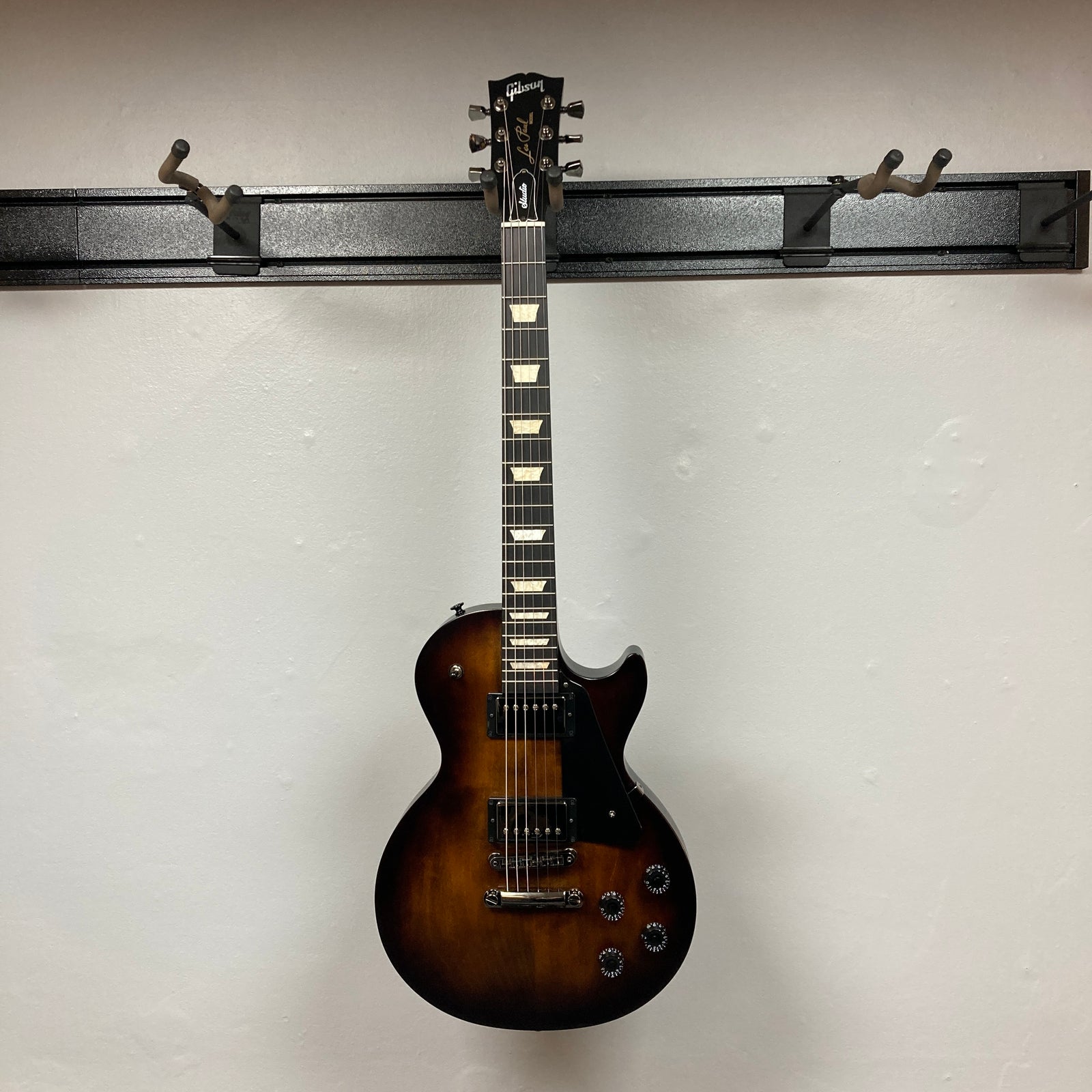 A 2025 Gibson Les Paul Studio Modern in Smokehouse Satin, featuring black pickups, four control knobs, a black pickguard, and photographed against a white background. Includes Gator Molded Case. A 2025 Gibson Les Paul Studio Modern in Smokehouse Satin, featuring black pickups, four control knobs, a black pickguard, and photographed against a white background. Includes Gator Molded Case.