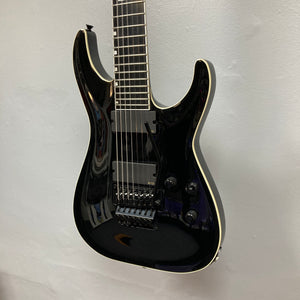 An ESP E-II Horizon FR-7 Black 7-string electric guitar with a gloss finish, white binding, humbuckers, Floyd Rose bridge, and three knobs hangs against a white wall. Comes with case.