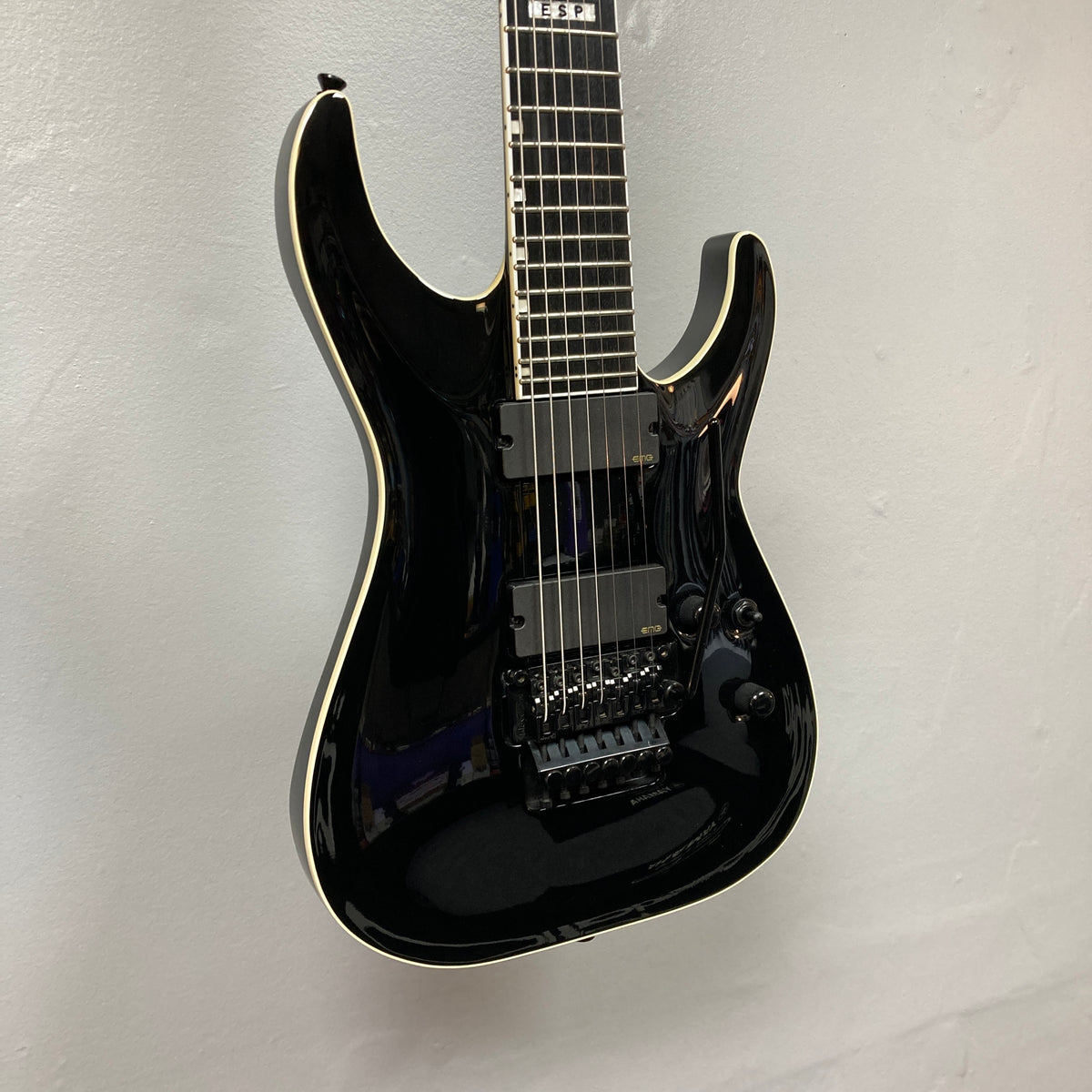 An ESP E-II Horizon FR-7 Black w/Case seven-string electric guitar with a Floyd Rose bridge and double-cutaway body hangs on a light-colored wall.