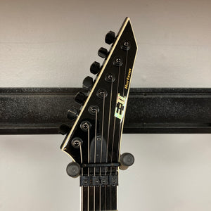 Close-up of the ESP E-II Horizon FR-7 Black w/Case by ESP, showing the 7-string electric guitar’s headstock with tuning pegs and locking nut, displayed on a wall hanger against a plain background.