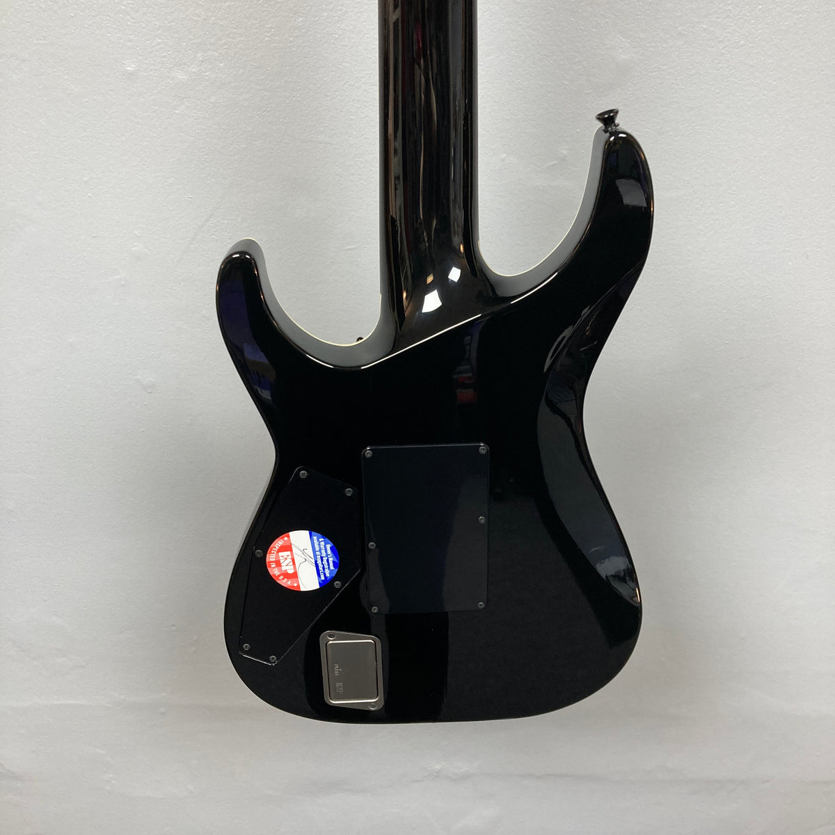Back view of an ESP E-II Horizon FR-7 Black w/Case 7-string electric guitar by ESP, featuring two rectangular panels and a round inspection sticker on the lower left, hanging against a white wall.