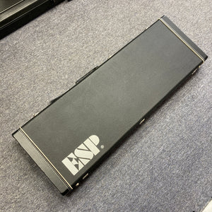 An ESP E-II Horizon FR-7 Black electric guitar with Floyd Rose bridge rests in its black ESP case featuring silver latches and a white ESP logo, displayed on a gray carpeted floor.