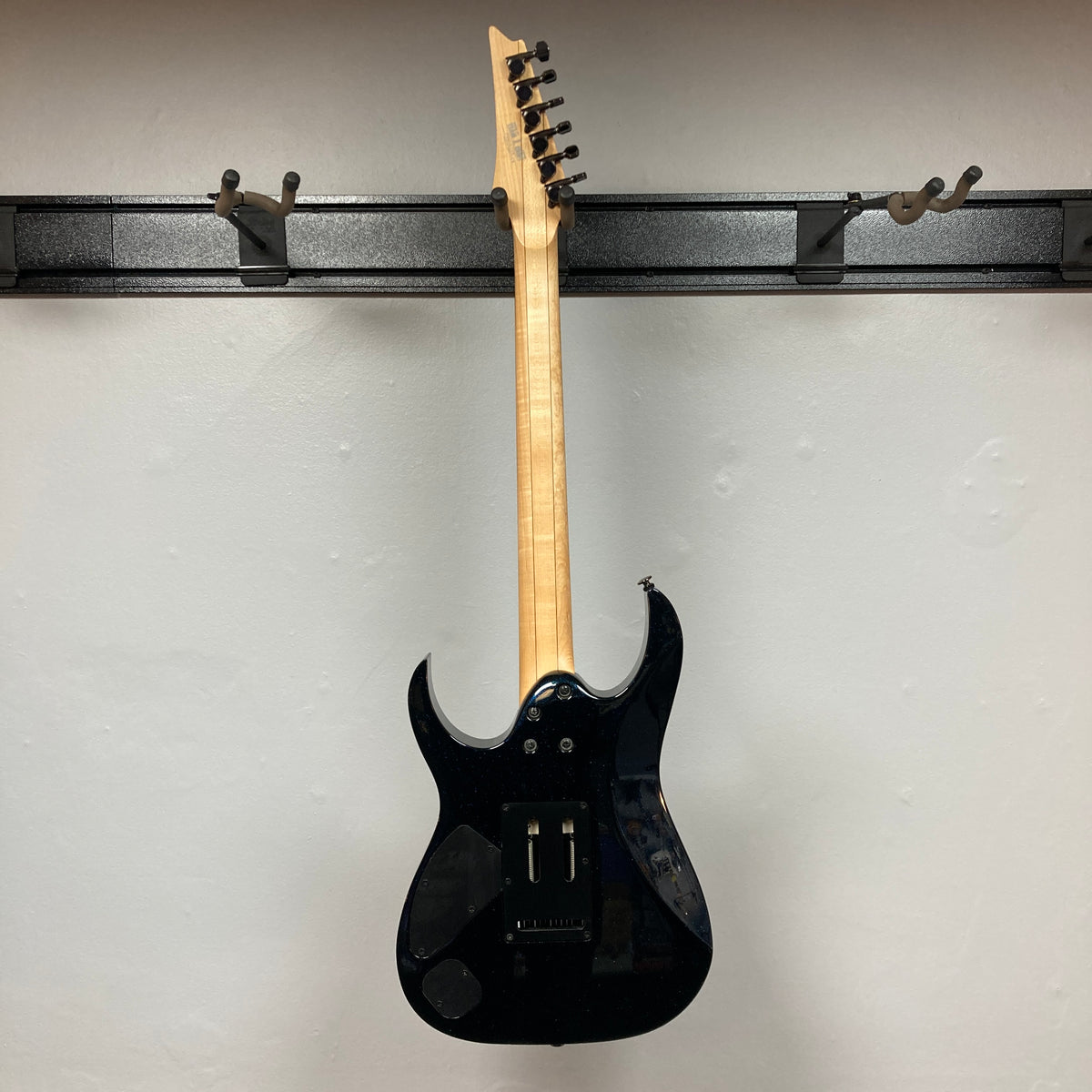 A Cosmic Blue Ibanez Prestige RG1570 electric guitar by Ibanez, shown hanging on a wall mount from the back, displays its tuning pegs, electronics cavity cover, and signature Wizard Prestige neck. Includes case.