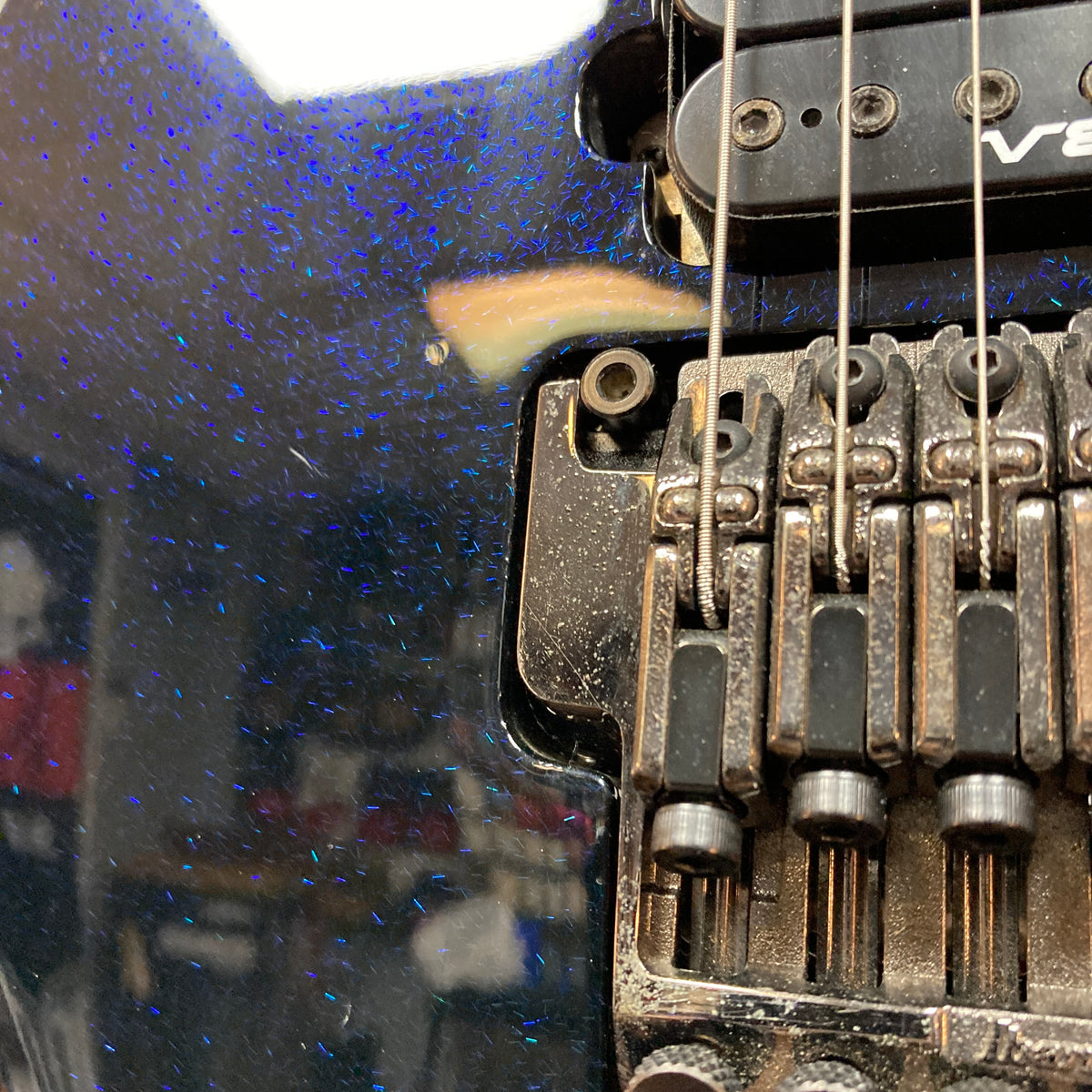 Close-up of the Ibanez Prestige RG1570 Cosmic Blue w/Case bridge, showing metal components, strings, dust, and wear on the blue-speckled finish of this Japanese-made electric guitar by Ibanez.