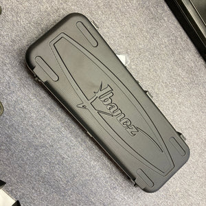An Ibanez Prestige RG1570 Cosmic Blue guitar with a black hard case featuring the Ibanez logo, ideal for this Japanese-made model, is shown resting on a gray carpeted floor.