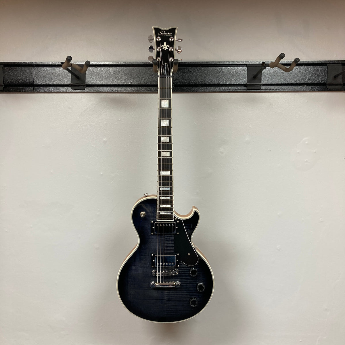 A Schecter Solo-II Custom Trans Black Burst w/Case Used by Schecter hangs on a wall-mounted rack against a plain white background.
