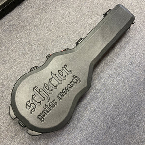 A Schecter Solo-II Custom Trans Black Burst with case, branded "Schecter," lies on a gray carpeted floor. The case is hard, black, and embossed with "Schecter guitar research," made to fit the Solo-II Custom model.
