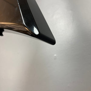 Close-up of the shiny black tip of a metallic object, likely from a Carvin 1992 Ultra V USA with Kahler Steeler Trem and MJ-wound Seymour Duncan DCJ, set against a plain light gray background.