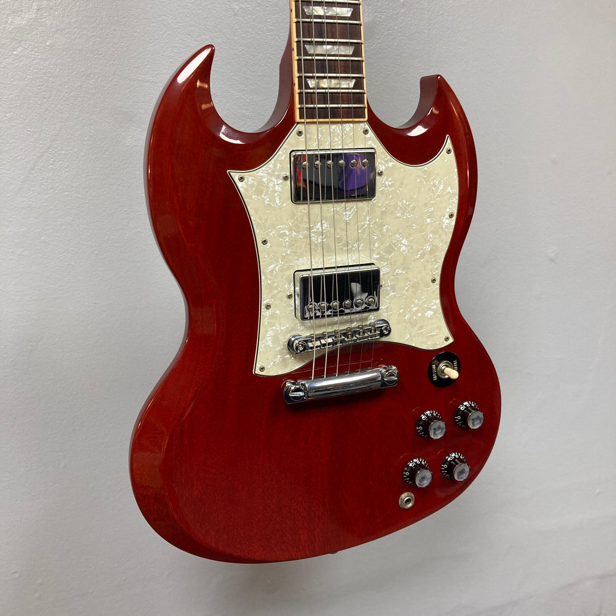 Gibson SG Standard Heritage Cherry yr 2000 Consign electric guitar with double-cutaway body, white pickguard, four control knobs, and chrome hardware by Gibson, made in USA and displayed against a light-colored wall.