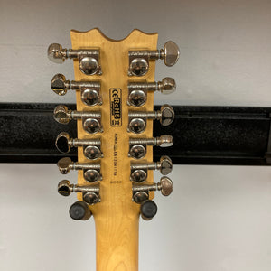 The back of a Dean Boca Trans Amber Burst 12 String w/Gigbag headstock by Dean shows twelve upward-facing tuning pegs and a serial number against a plain background.