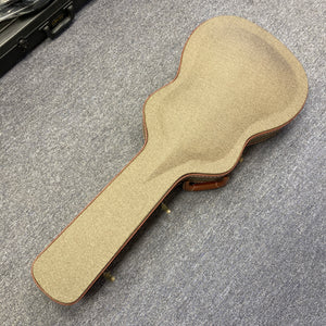 A Guild Gad-30reasb acoustic-electric guitar crafted from solid Indian rosewood rests inside its closed, tan-colored Guild case with brown trim on a gray carpeted floor.