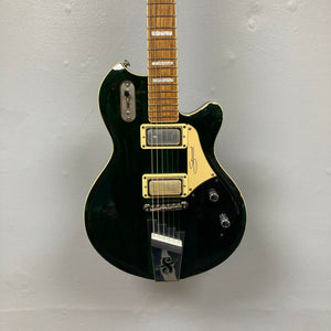 A Supro 1296 Silverwood in British Racing Green, featuring two Gold Foil pickups, a gold pickguard, and chrome hardware, is hanging against a light gray wall.