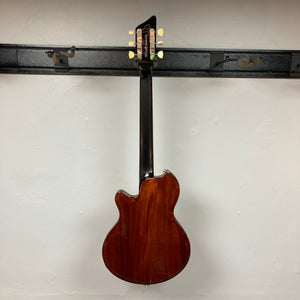 A Supro 1296 Silverwood electric guitar in British Racing Green, complete with gig bag, hangs on a black wall-mounted rack and is photographed from the back against a plain white wall, showcasing the elegant styling characteristic of Supro instruments.