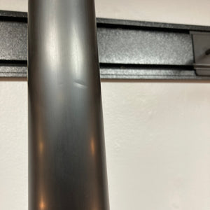 Close-up of a black metal pole with a small dent, set against a wall-mounted black horizontal rail and a white background—evoking the sleek lines and finish of the Supro 1296 Silverwood British Racing Green w/Gigbag guitar by Supro, known for its Gold Foil pickups.