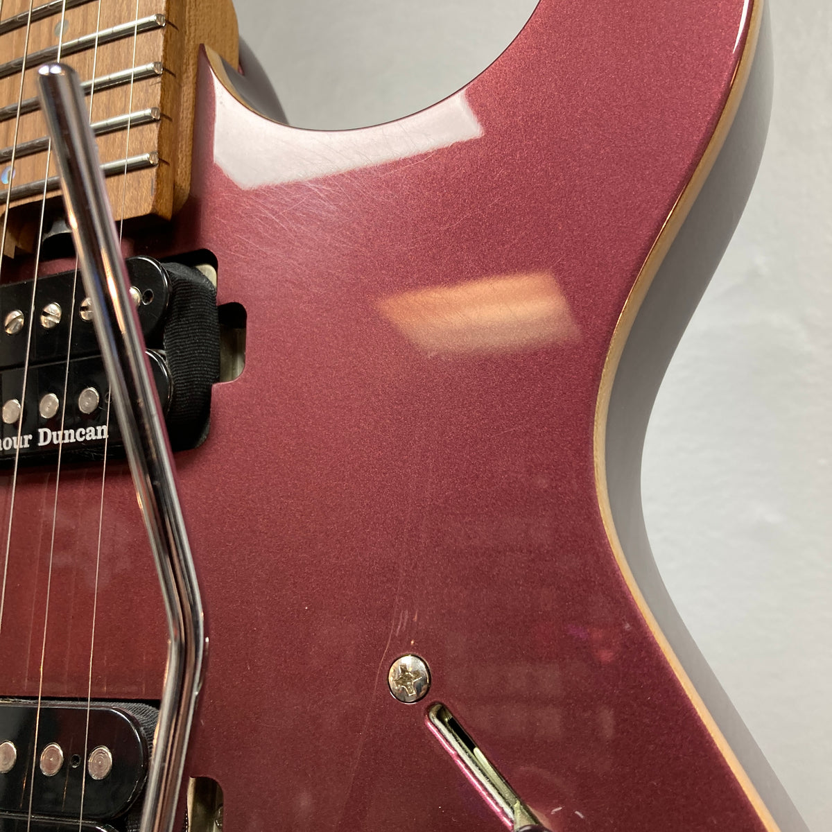 Close-up of the Cort FW-G300 PRO Vivid Burgundy electric guitar body, featuring its pickups, strings, whammy bar, and part of the neck against a plain light-colored wall.