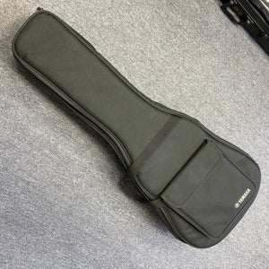 A Yamaha A3M ARE Vintage Natural Acoustic Guitar by Yamaha, featuring a solid Sitka spruce top and SRT2 pickup system, along with its included hard bag, is resting on a gray carpeted floor. The hard bag offers a convenient front pocket for storing accessories.
