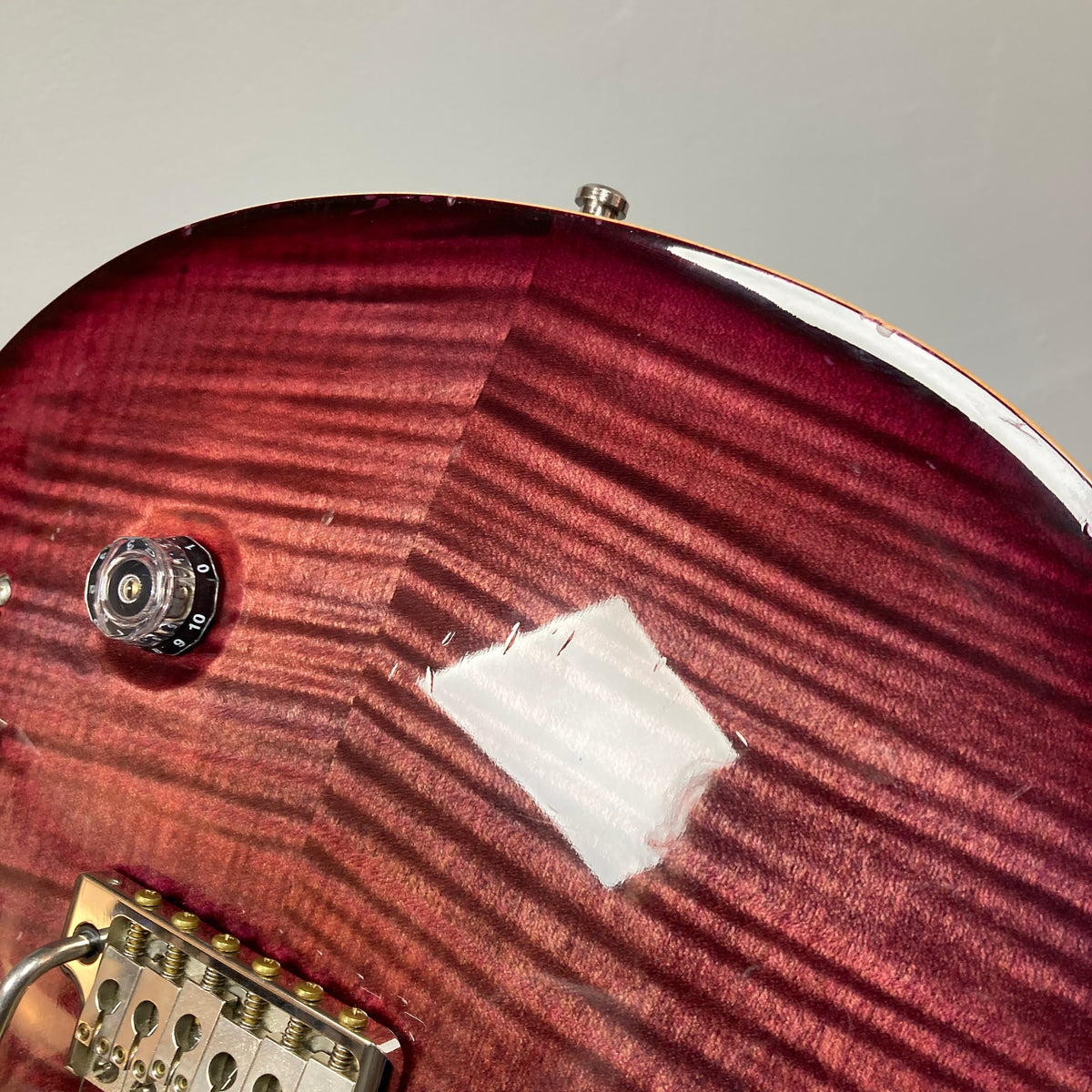 Close-up of a PRS Custom 24 Violet 2011 electric guitar body, showcasing the wood grain, control knob, bridge, and a noticeable area of chipped or worn finish near the top edge. The image highlights PRS’s attention to detail and features such as the 59/09 humbuckers.