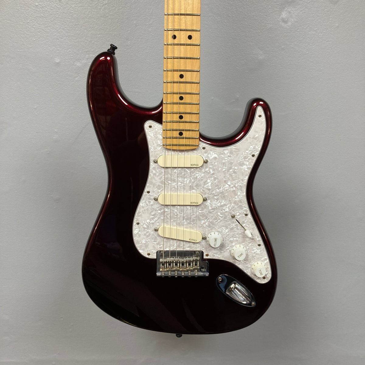 Fender American Standard Strat upgraded Gilmour EMG DC-20 Bordeaux Metallic electric guitar with a dark red Bordeaux Metallic finish, three EMG DG20 David Gilmour pickups, white pickguard, and maple neck hanging against a plain gray wall.