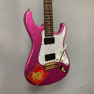 Edwards ESP E-SN-185-TO Takayoshi Ohmura Twinkle Pink electric guitar, featuring dual humbuckers, a sparkling pink glitter finish, white pickguard, gold hardware, and a red decorative sticker in the lower corner, photographed against a plain gray wall.