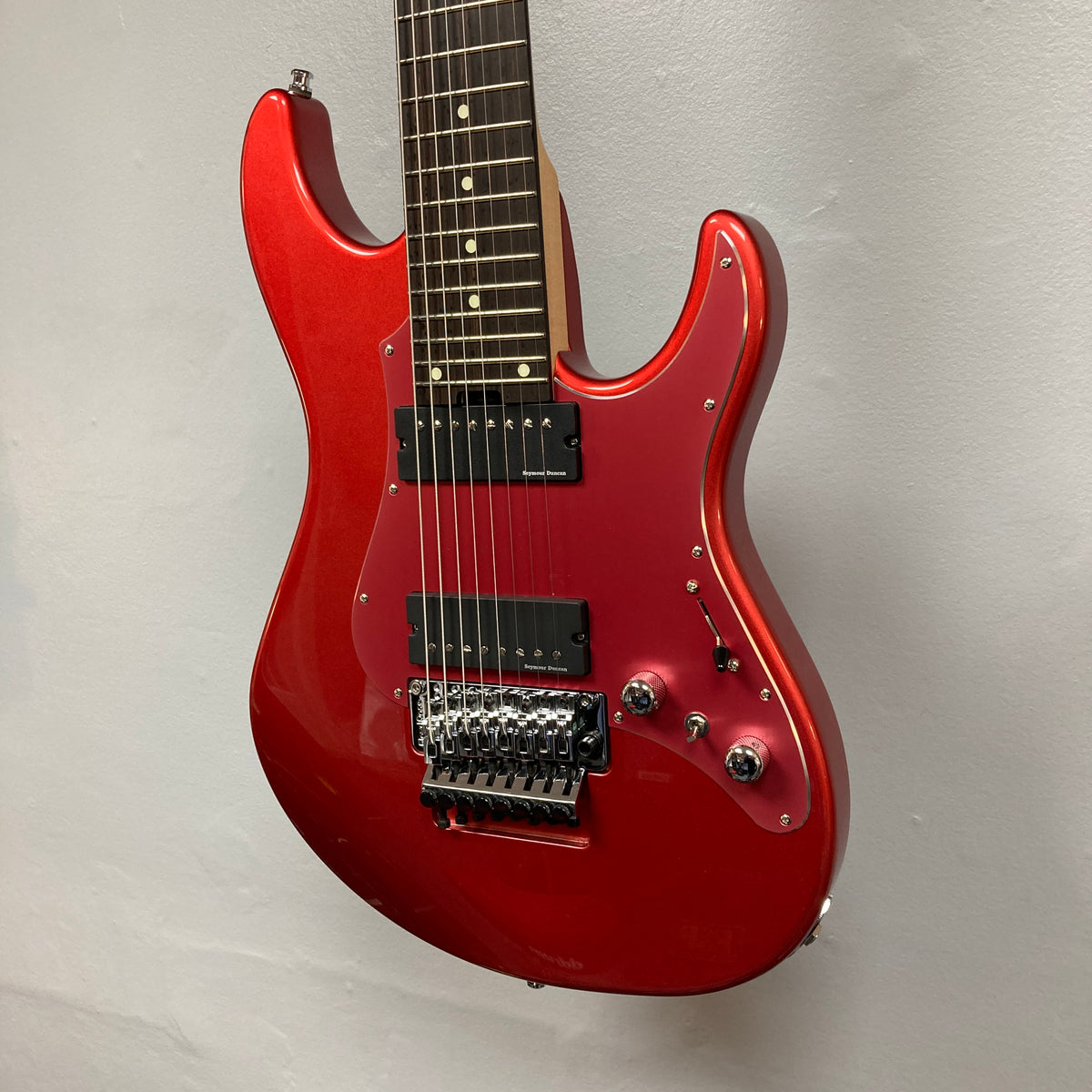 An ESP Snapper Raiden 8 ISAO Custom eight-string guitar by ESP, featuring two humbucker pickups, a Floyd Rose tremolo bridge, and two control knobs, is hanging against a light gray wall.