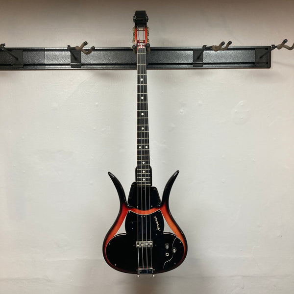 The 1966 Ampeg ASB-1 Devil Bass (Serial #531) is a vintage electric bass guitar featuring a striking sunburst finish and unique horned body shape inspired by the iconic Ampeg design. This classic model comes equipped with three control knobs, a black pickguard, and a bridge-mounted transducer pickup for enhanced tonal versatility. Includes case.