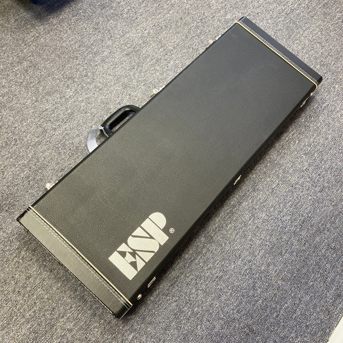 A black rectangular Edwards guitar case, designed to fit the Edwards E-SN7-194MF Mikio Fujioka Signature seven-string guitar, with a handle, placed on a gray carpeted floor.