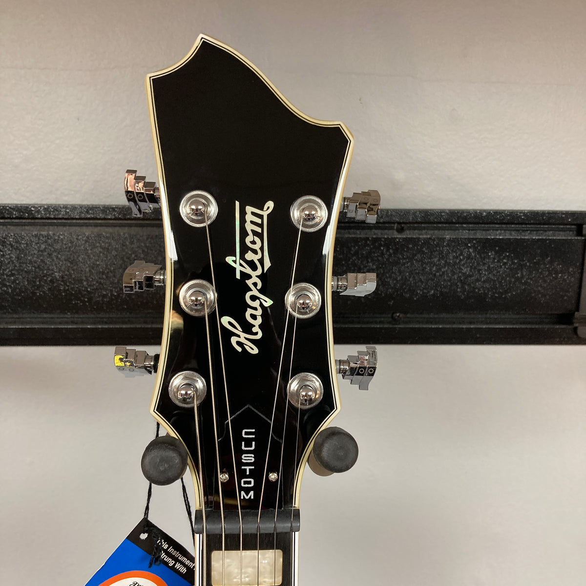 The headstock of the Hagstrom Fantomen Custom Black w/case electric guitar by Hagstrom features six tuning pegs, a silver logo, and “CUSTOM” written vertically.