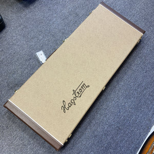 A rectangular Hagstrom guitar case featuring a beige textured surface with brown edges rests closed on a gray carpeted floor, ready to securely protect your prized Hagstrom Fantomen Custom Black electric guitar.