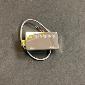 A Godin Neck Humbucker pickup with a nickel cover (model GAHN1), featuring attached wires and designed to enhance sound, is placed on a black surface.